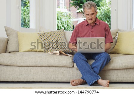 Middle aged man sitting on sofa and using laptop at home