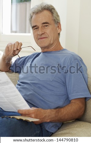 Portrait of a middle aged man holding spectacles and bill at home