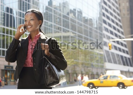 Smiling African American businesswoman using mobile phone on street against building