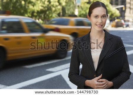 Portrait of a confident young businesswoman holding portfolio on street