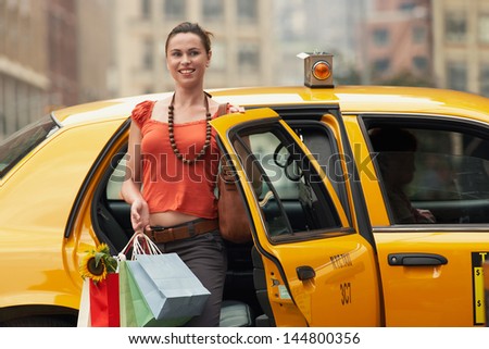 Portrait of a smiling young woman with shopping bags exiting yellow taxi