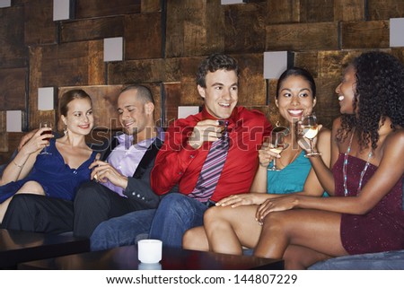 Group of multiethnic friends sitting on couch with drinks in bar