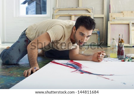 Young male artist looking at canvas on studio floor