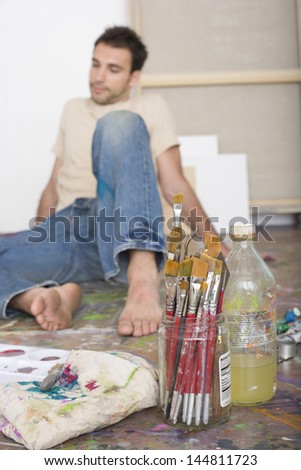 Male artist sitting with painting tools on floor at a studio