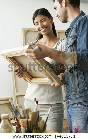 Happy multiethnic couple looking at canvases in artist studio
