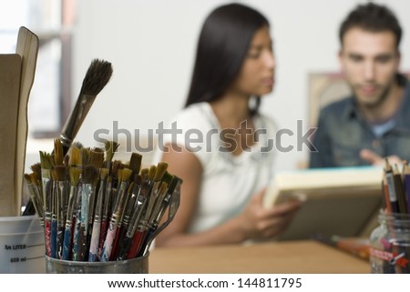 Blurred multiethnic couple looking at canvases in artist studio
