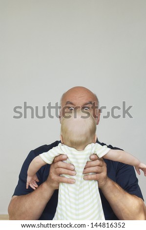 Grandfather holding up grandchild in front of him - stock photo