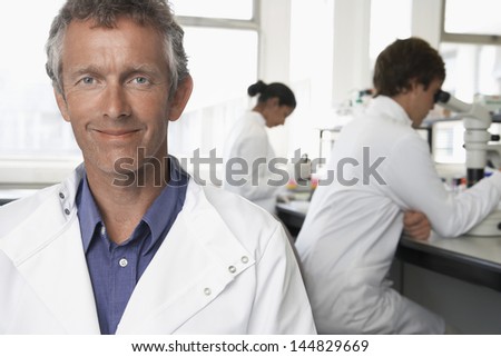 Portrait of happy male scientist with colleagues working in background