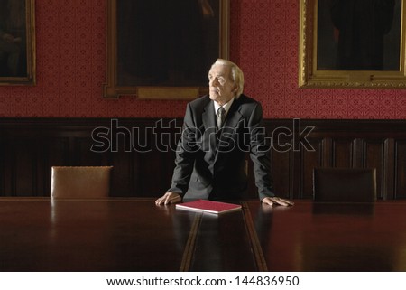 Thoughtful senior businessman leaning hands on conference table