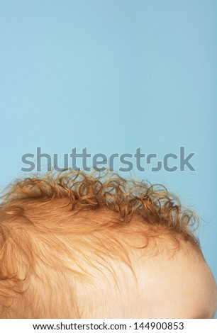 Cropped image of baby\'s head with red curly hair on blue background