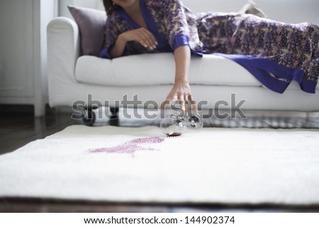 Midsection of woman reaching toward spilled wine glass on rug