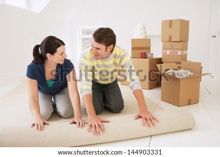 Happy young couple unrolling carpet in new home