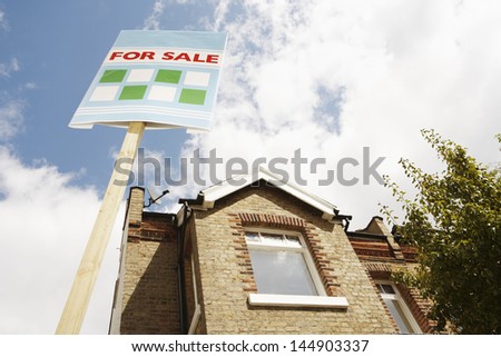 Low angle view of sale sign in front of new house against cloudy sky