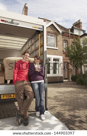 Full length portrait of young couple standing by moving van in front of new home