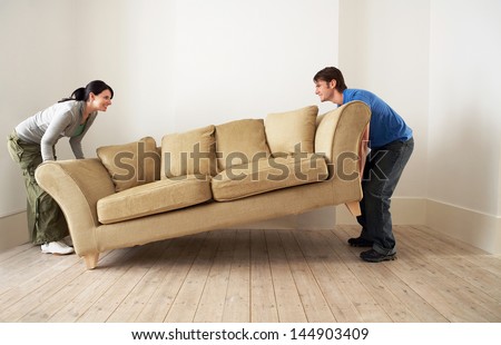 Side view of happy young couple placing sofa in living room of new home