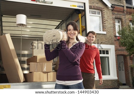 Portrait Of Happy Young Couple Carrying Rolled Carpet By Moving Van