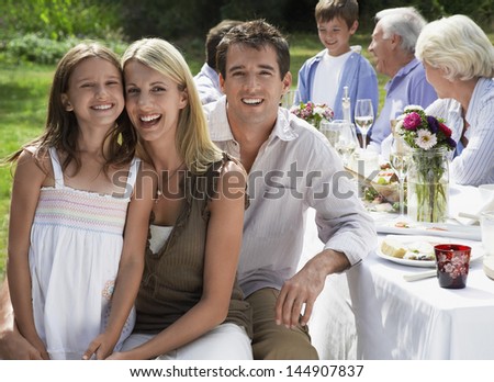 Portrait of happy parents with daughter at dining table with family in background