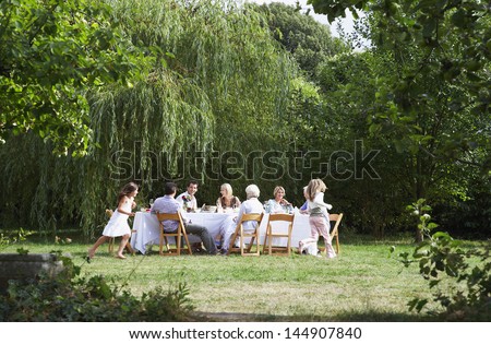 Happy family sitting at dining table while girls running around in garden
