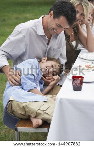 Father and son having fun while dining with family in garden
