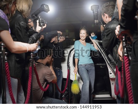 Excited woman with cleaning equipment getting out of limousine in front of paparazzi