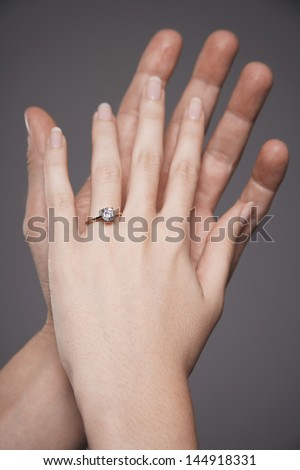 Closeup of hands together showing woman\'s engagement ring against gray background
