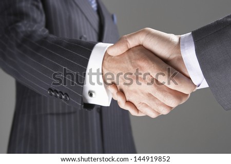 Closeup of two businessmen shaking hands against gray background
