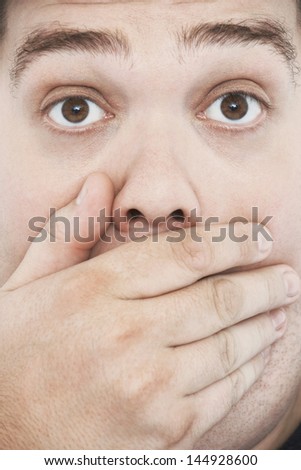 Extreme closeup portrait of an overweight man with hand on mouth and raised eyebrows