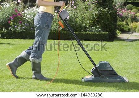 Side view of a woman mowing the lawn with electric mower