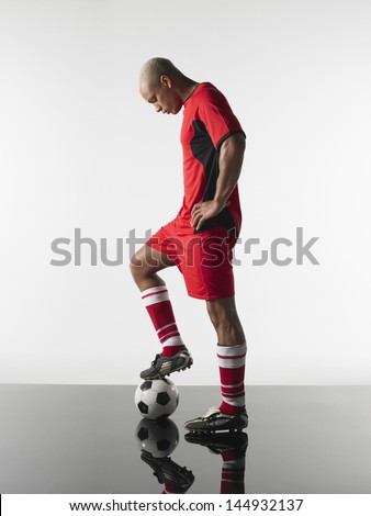Full length side view of a player with leg on football against white background