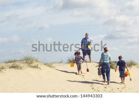 Rear view of family walking up sand dune on beach against the sky