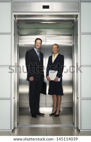 Happy business colleagues looking away while standing in elevator