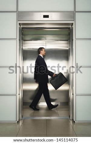 Profile shot of middle aged businessman with briefcase walking in elevator