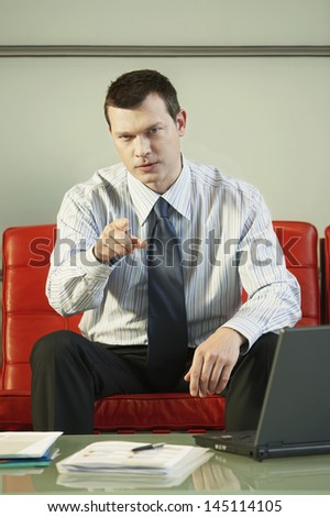 Portrait of confident middle aged businessman pointing while sitting on red couch in office