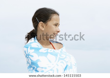 Happy little preadolescent girl wrapped in towel looking away while standing at beach