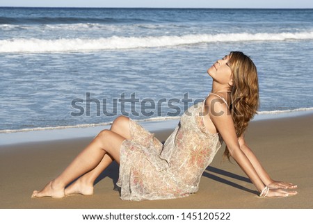 Side view of beautiful young woman looking away while sitting on sand dune at grassy beach