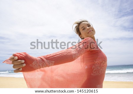 Side view of beautiful young woman looking away while sitting on sand dune at grassy beach