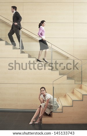 Young businesswoman looking away while using cellphone with colleagues climbing stairs in office