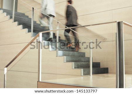 Blurred Motion Of Businessmen Moving Up Stairs In Office