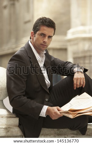 Portrait of confident young businessman holding newspaper outdoors