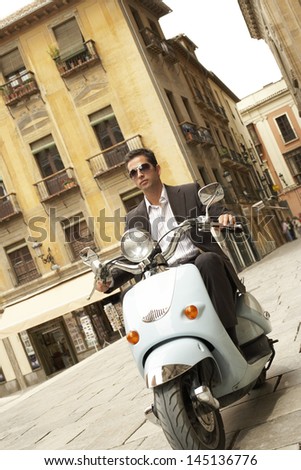 Handsome young businessman riding scooter through town
