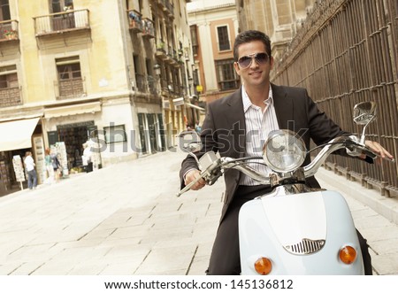 Portrait of handsome young businessman riding scooter through town