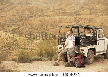 Middle aged couple in back of four-wheel-drive car on cliff edge in desert