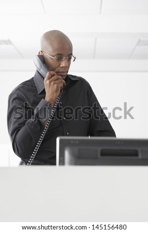 Serious African American businessman using telephone at computer desk