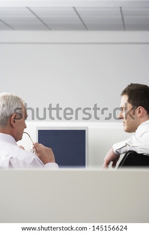 Rear view of business people sitting at computer desk in office cubicle