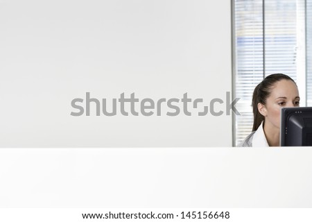 Serious young businesswoman using computer in office cubicle