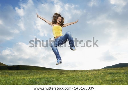 Young woman with arms outstretched screaming while jumping in park