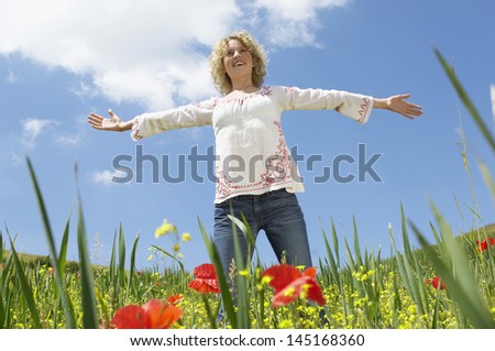 Low angle view of young woman with arms outstretched standing in poppy field
