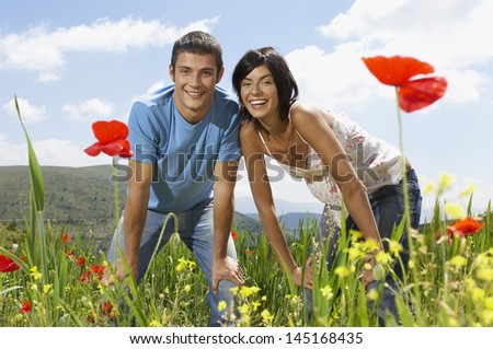 Portrait of young multiethnic couple with hand on knee in poppy field