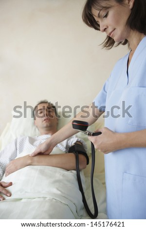 Cropped nurse taking blood pressure and pulse of patient in hospital bed