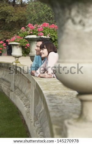 Side view of a smiling couple looking over wall by potted plants